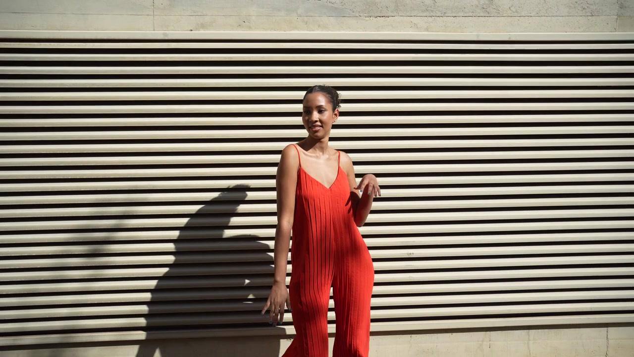 A stylish woman in a beautiful red dress posing gracefully against a modern wall setting