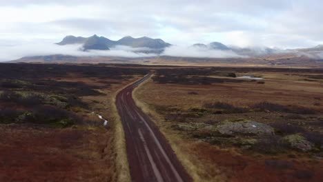 Aerial-view-following-long-curving-rural-road-towards-misty-Snæfellsnes-mountain-range-skyline,-Iceland