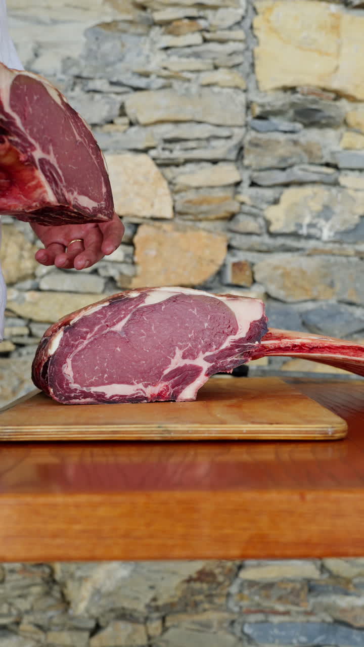 Chef hand picking fresh raw beef ribeye on wooden board in kitchen vertical view, close-up of premium marbled meat preparation for cooking or grilling