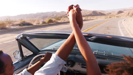 Una-Pareja-En-Un-Auto-Descapotable-Se-Toma-De-La-Mano-En-El-Aire,-Vista-Elevada