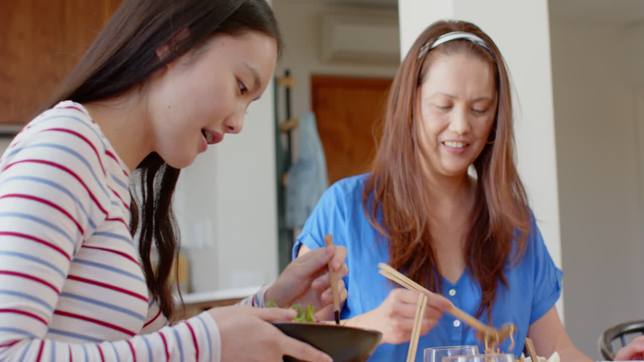 Eating together, asian mother and daughter enjoying meal with chopsticks at home dining table