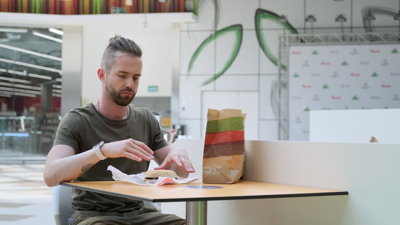Man äter en hamburgare i en gallerias food court