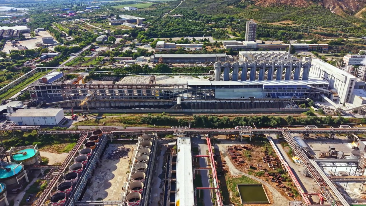 Vista de un gran complejo industrial con edificios, tanques y tuberías en un área circundante con vegetación y colinas al fondo