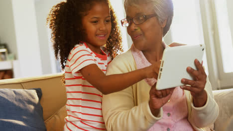 smiling grandmother and granddaughter using digital tablet on sofa in living room 4k