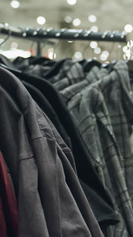 clothing store showcasing a variety of clothes on hangers, including shirts and jackets, with a blurred background. captured with a handheld camera, the video highlights the organized display