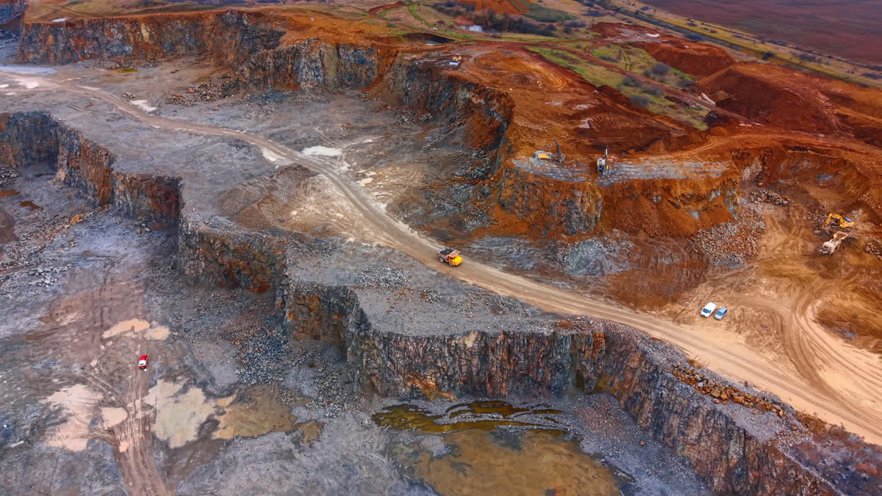 Mining operation in a remote area. Machines move on dirt roads in a large mining site with rocky terrain. Workers focus on extracting minerals below