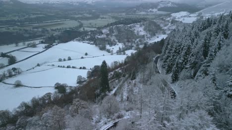 Paisaje-Nevado-De-Invierno-Con-La-Ladera-Del-Bosque-Y-Cámara-Panorámica-Hacia-Abajo-Mostrando-El-Coche-Viajando-Por-Una-Carretera-Oscura