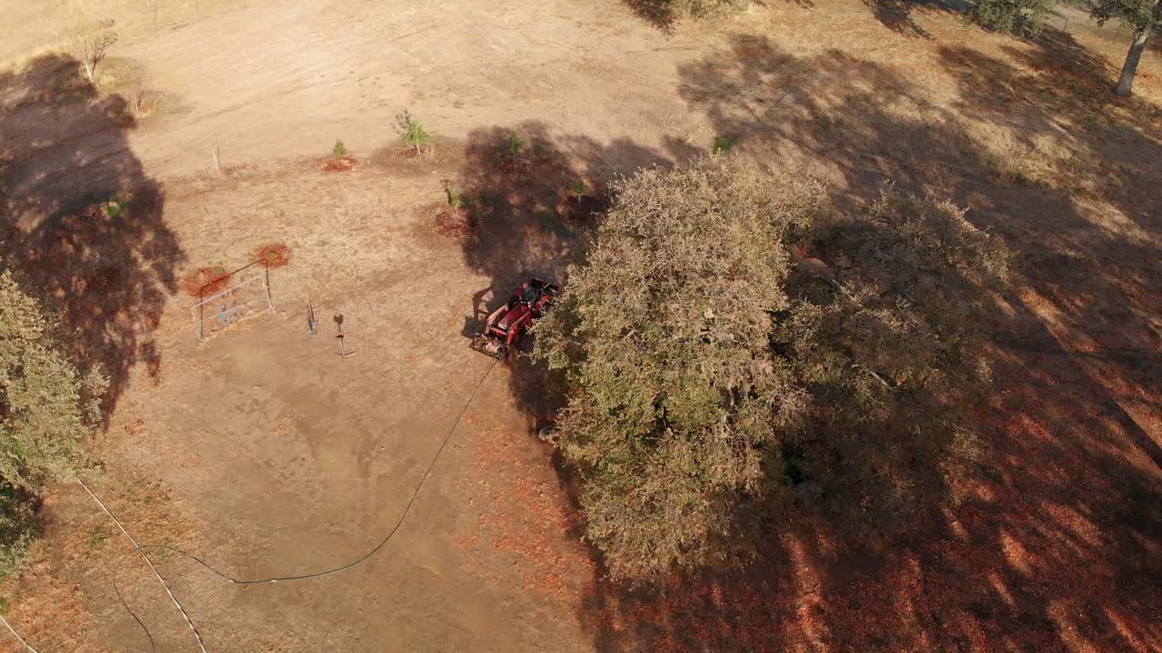 Sorvolo aereo con drone con panoramica su un trattore rosso che scarica legna da ardere in una fattoria rurale