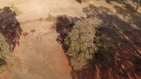un avión no tripulado vuela sobre un tractor rojo arrojando leña en una granja rural