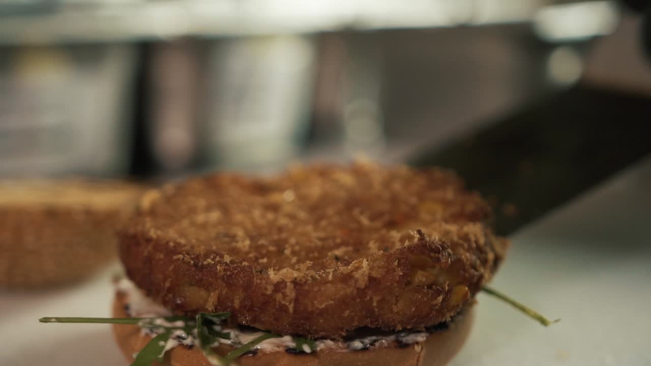 Close-up of chef hands wearing black glove adding burger on bread. Slow-motion
