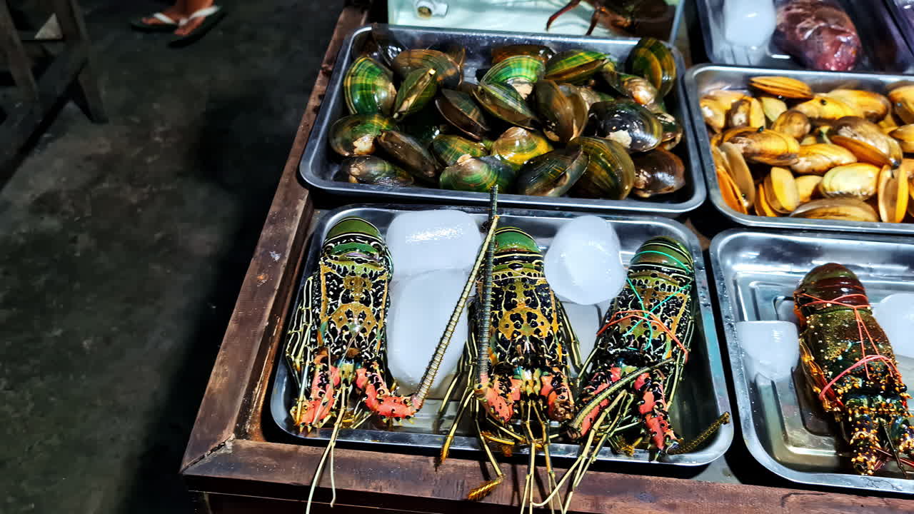 Person points to seafood items like lobsters, mussels, and clams at busy fresh market display