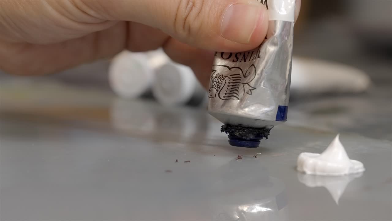 Hand holds and squeezes a blurb of purple blue oil paint