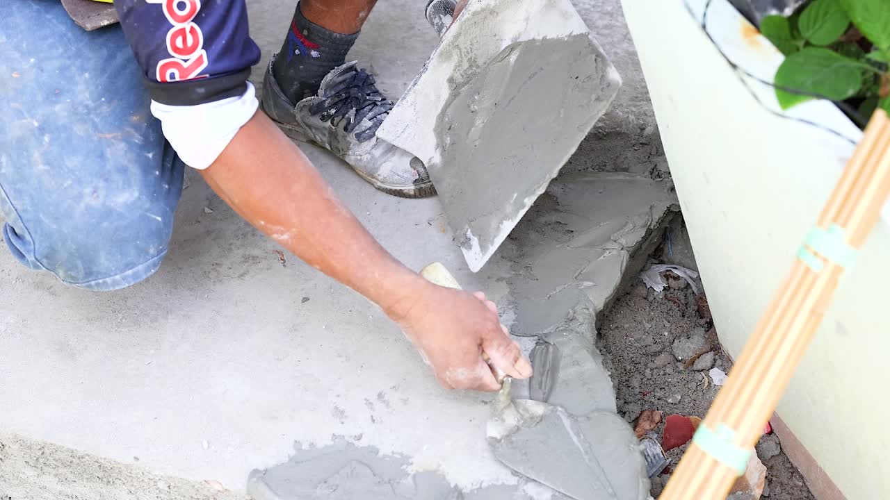 A worker skillfully applies and smooths concrete on a surface in Phuket, Thailand, under natural daylight conditions
