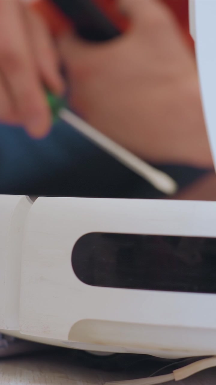 Close up shows hands using screwdrivers to service bottom part of small white electronic device likely for repair. focus remains on tool interaction without revealing broader context