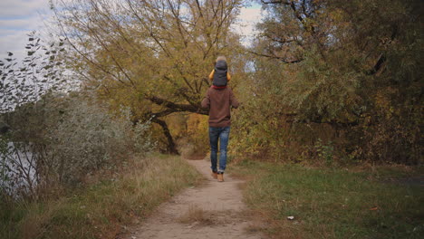 Vater-Trägt-Seinen-Kleinen-Sohn-Auf-Schultern-Und-Geht-An-Einem-Herbsttag-Im-Wald-Spazieren,-Nachdem-Er-Am-Wochenende-Eine-Familienpause-In-Der-Natur-Gemacht-Hat.-Vaterschaft-Und-Kindheit