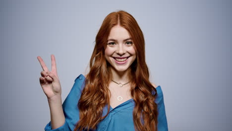 vriendelijke roodharige vrouw die een vredesteken doet binnen. vrolijk meisje dat in de studio poseert