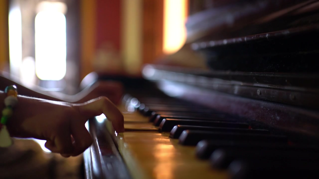 Un primo piano mostra le dita di un ragazzo che suonano i tasti di un pianoforte molto vecchio, vintage.