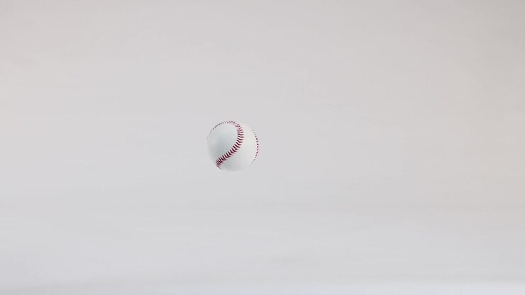 Una palla da baseball bianca cade e rimbalza ripetutamente su uno sfondo bianco pulito da studio, al rallentatore