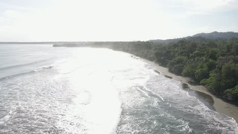 AERIAL---Drone-flies-over-ocean-along-shoreline-of-green-jungle