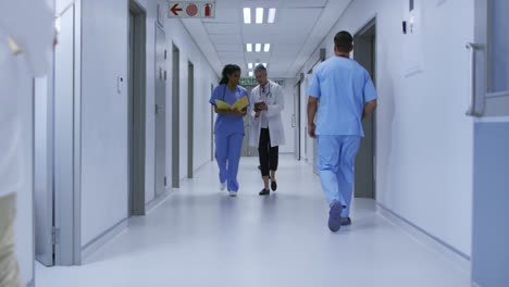 duas médicas diversas caminhando no corredor do hospital, olhando para o tablet e o arquivo e falando