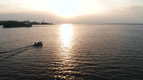 Kleines-Boot,-Das-In-Richtung-Sonnenuntergang-Rast-Und-An-Einem-Containerschiff-Vorbeifährt