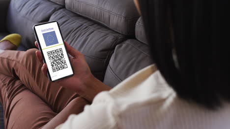 mujer en casa con un teléfono inteligente con certificado de vacunación contra la covid, bandera de la ue y código qr en la pantalla