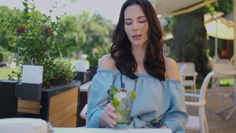 beauiful woman sitting in outdoor restaurant and sip mojito dring in summer hot day