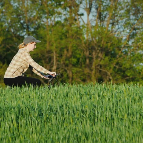 Pan-Shot:-Woman-Rides-Her-Bike-Among-Green-Wheat-Fields