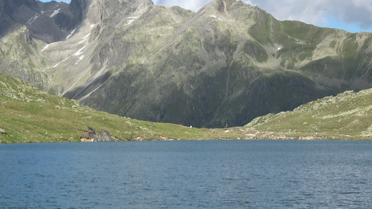 Ampia inquadratura del Lago Merjelen con acqua blu calma e aspre cime alpine sullo sfondo, un suggestivo paesaggio estivo vicino al Ghiacciaio dell'Aletsch nel Vallese, Svizzera.