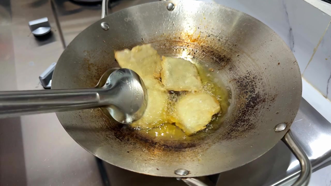 Close up of frying tempeh in hot oil with tongs, traditional Indonesian cooking, homemade food preparation concept.