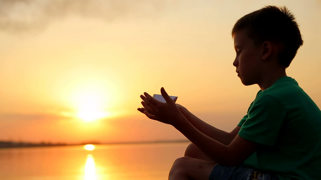 Boy Launching Paper Boat. Little boy launching paper boat on water from beach