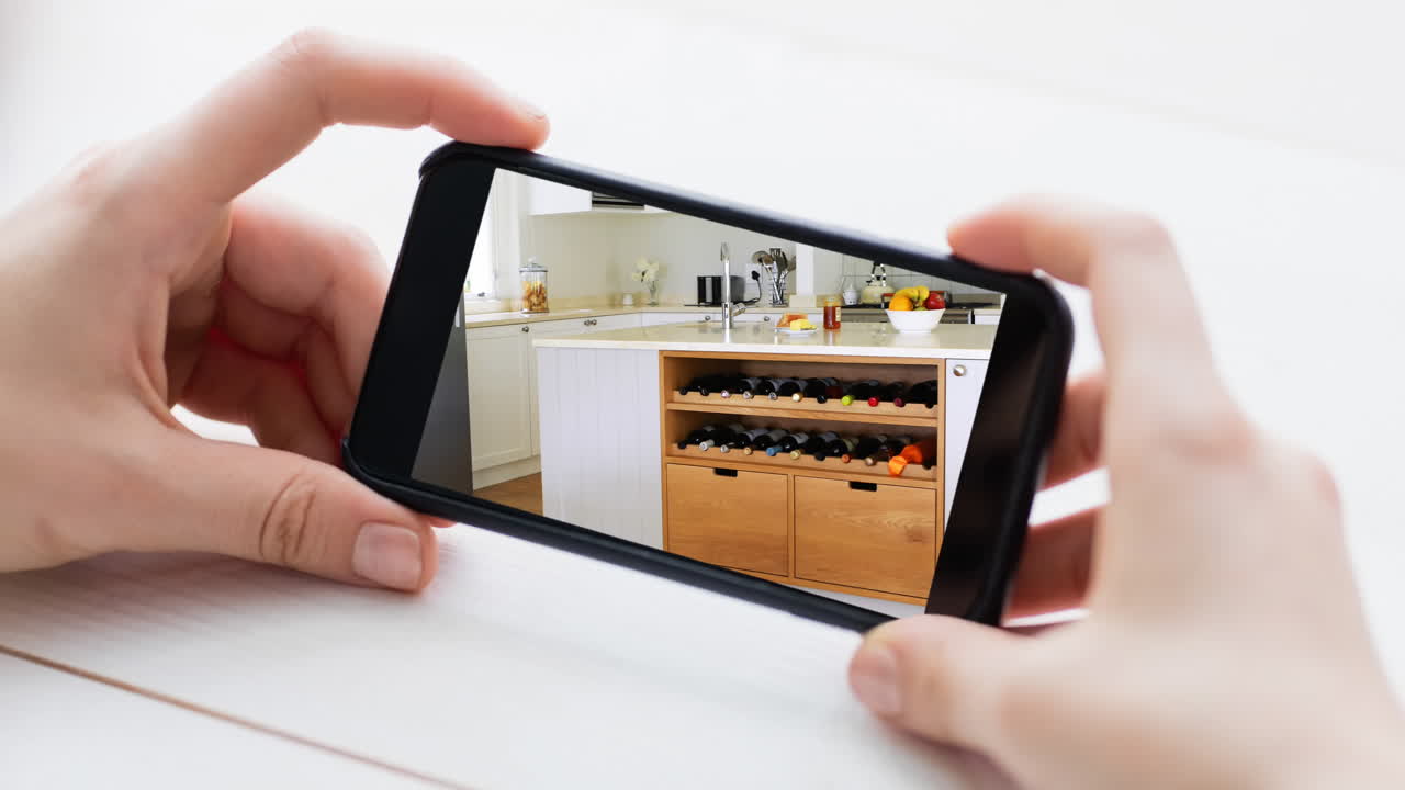 persona que sostiene un teléfono inteligente con interiores de cocina modernos mostrados en la pantalla