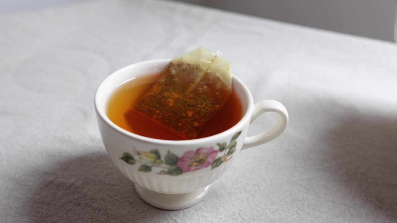 Bolsita de té infusionándose en agua caliente dentro de una taza de té floral.