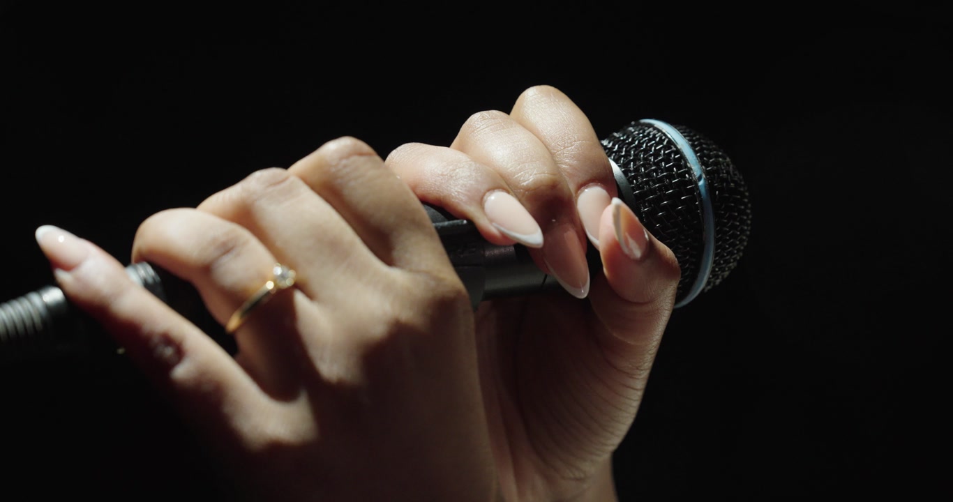 Close-up of hands adjusting a microphone on a black background. Concept of music, performance, audio setup and stage preparation.