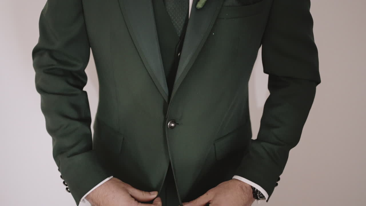 어두운 초록색 의상을 입은 남자가 재을 조정하고, 부토니에를 입고, 이벤트를 준비하고 있습니다.