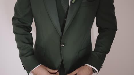 Man-in-a-dark-green-suit-adjusting-his-jacket,-wearing-a-boutonniere,-preparing-for-an-event