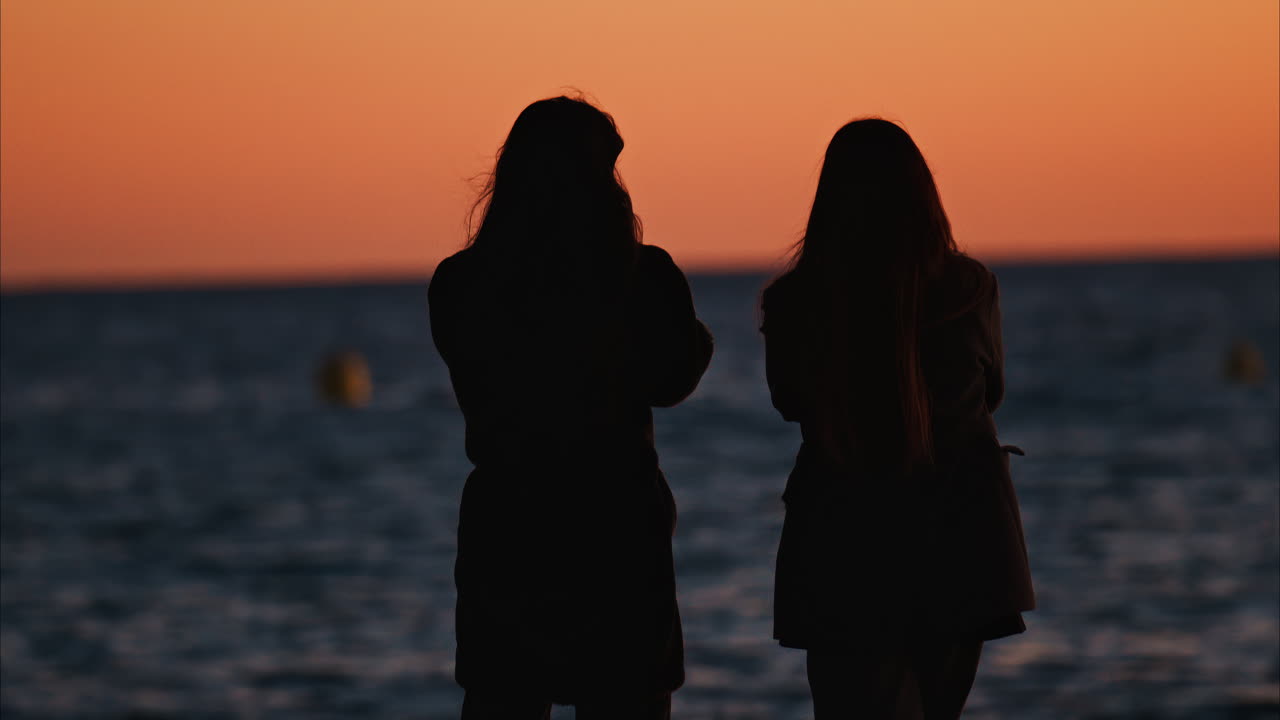 Two women on the beach and looking at the sea at sunset