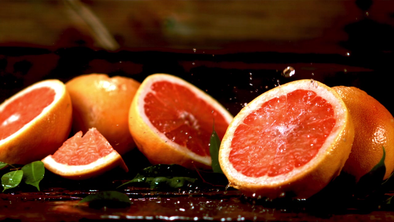 Gocce d'acqua che schizzano su mezzi e fette di pompelmo rosso fresco.