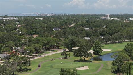 Aerial view of Florida golf course, lush fairways, nearby homes, scenic pond, coastal skyline, and blue skies—perfect blend of leisure, nature, and suburban lifestyle