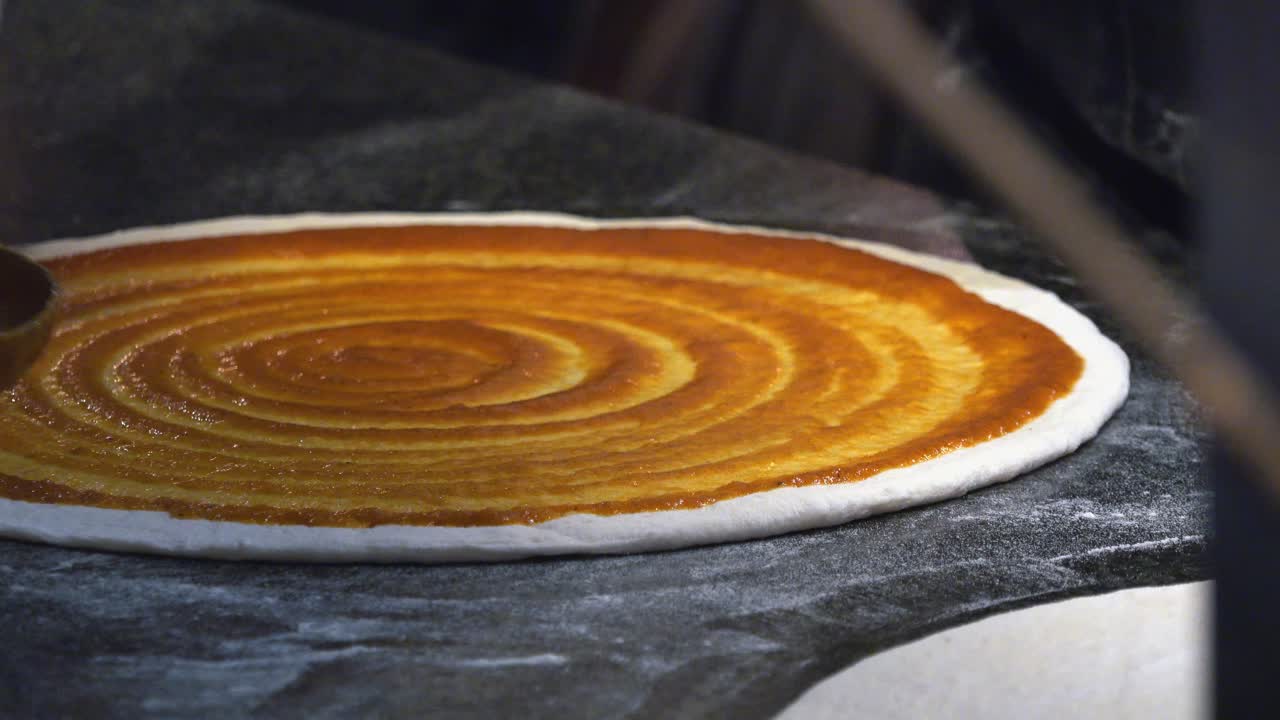 Pizzaiolo che applica salsa di pomodoro alla base della pizza