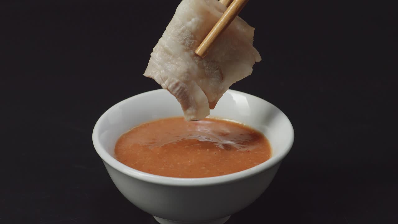 검은색 배경에 가락으로 샤부 샤부 디프 소스에 담긴 베이컨 돼지고기의 클로즈업