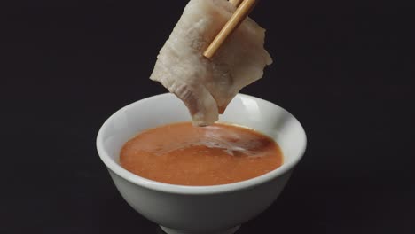 cerca de la carne de cerdo de tocino sumergida en la salsa de salsa de shabu shabu por palillos sobre el fondo negro