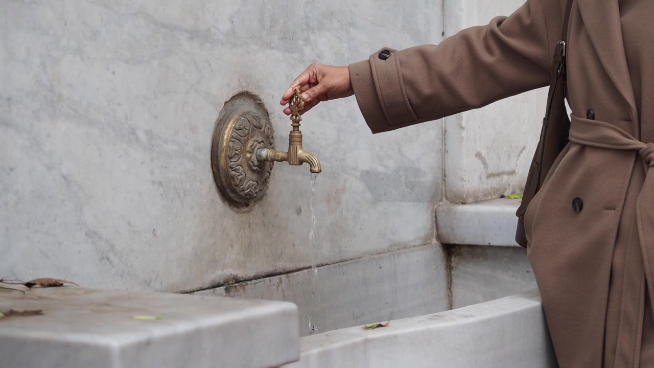 Person Turning Off Antique Brass Faucet at Marble Fountain