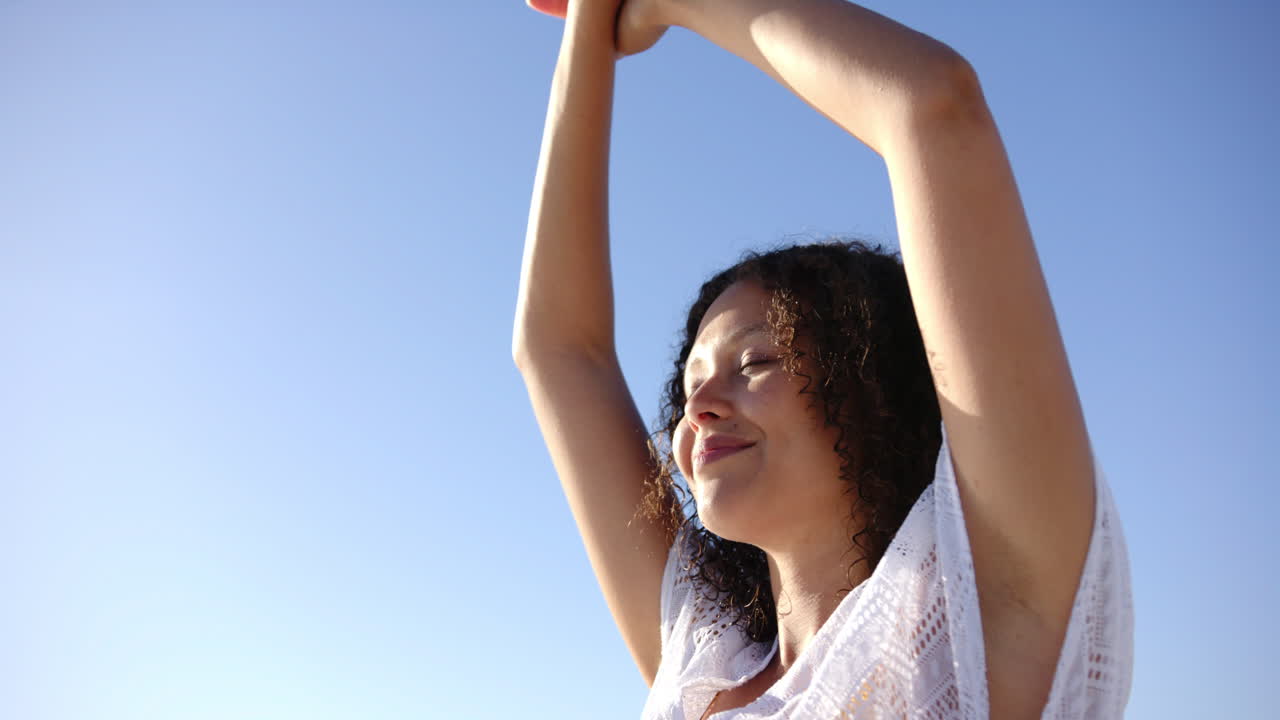 una joven de dos razas con el cabello rizado extiende sus brazos contra un cielo azul claro