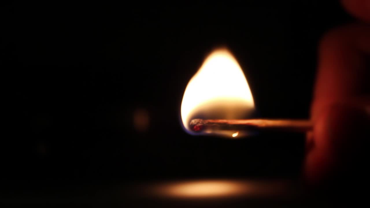 Primer plano de una cerilla encendiéndose y ardiendo en la oscuridad.