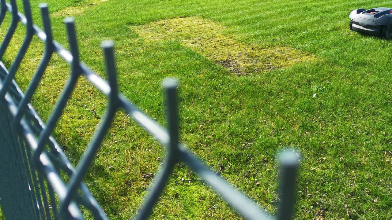 Robotic Husqvarna lawn mower behind fence on mowing grass