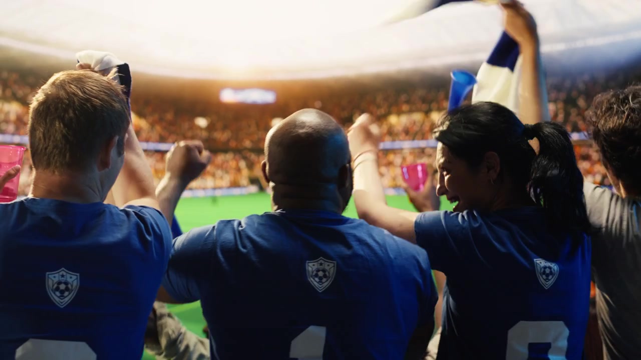 Aficionados al fútbol gritan con los brazos levantados en un estadio deportivo.