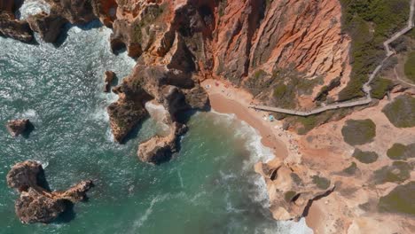 board walk down to beach ocean ripples of ponta da piedade and praia da dona ana, drone top view