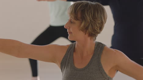 Clase-De-Yoga-Mujer-Madura-Ejerciendo-Un-Estilo-De-Vida-Saludable-Practicando-Pose-De-Guerrero-Disfrutando-De-Un-Entrenamiento-Físico-En-Grupo-En-El-Estudio