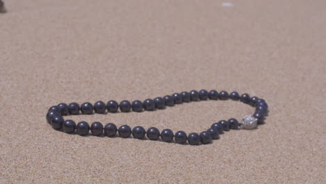 moving around a perl jewellery necklace on sand slow motion 120 fps shot